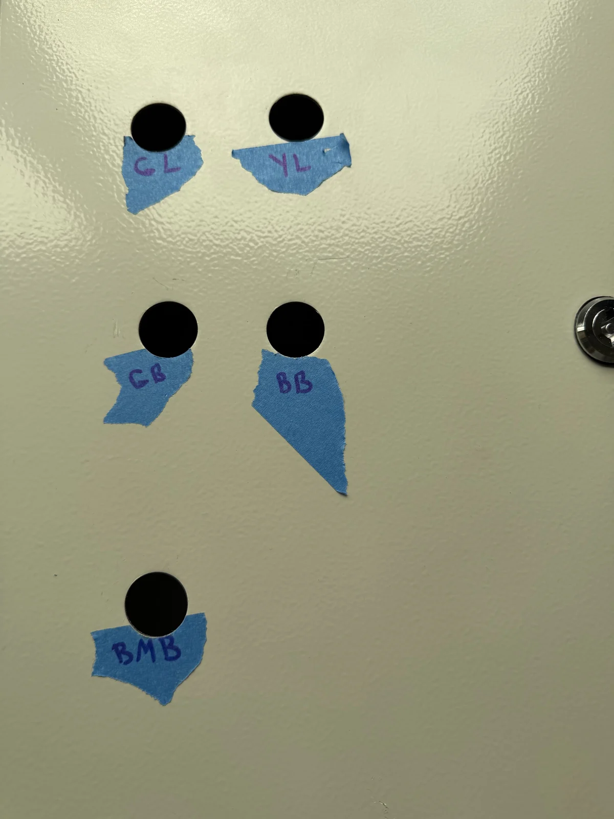 Cabinet door with five punched holes and temporary blue tape labels